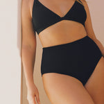 Angled view of black textured triangle bikini top on model, showing structured cup and wider shoulder strap detail.