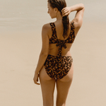 back view of noir hibiscus floral bikini top with adjustable tie-back and mid-rise matching bottom on the sand
