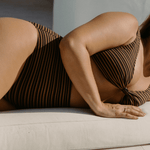 model wearing mocha stripe bikini top and high waisted bottoms laying down in relaxed sunlight