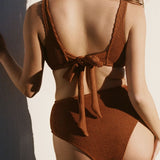 Back shot of wearing brown rust caramel D+ bikini top and high waisted bikini bottom in textured fabric with tie back. 