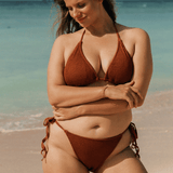 Woman in a brown triangle halter bikini standing on a beach with ocean in the background