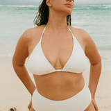 Woman in a white high waisted bridal bikini standing on a beach with ocean in the background