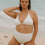 Woman in a white high waisted bikini standing on a beach with ocean in the background