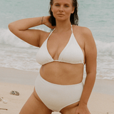 Woman in a white high waisted bikini standing on a beach with ocean in the background