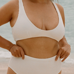 Woman in a white high waisted bikini standing on a beach with ocean in the background