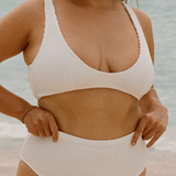 Woman in a white high waisted bikini standing on a beach with ocean in the background